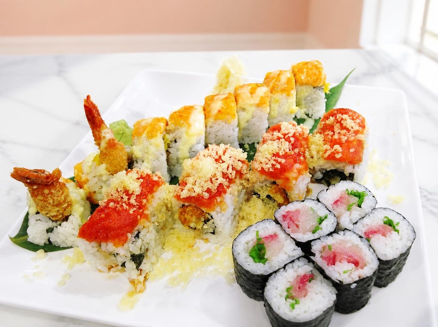 A white platter of Sushi Kola rolls topped with tempura crunch, spicy sauce and shrimp