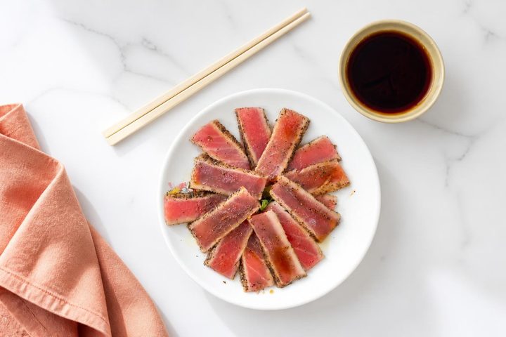 Thin slices of pepper-seared tuna with soy sauce and chopsticks